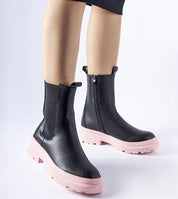 Black ankle boots with pink soles and side zippers, worn with a skirt, showcasing modern design and comfort for winter fashion.