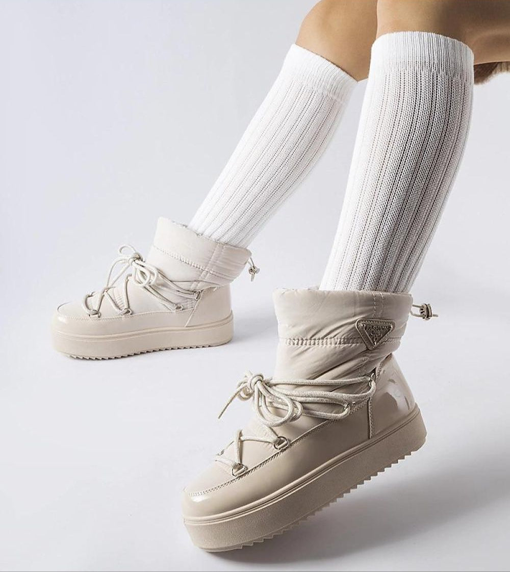 Person wearing Tharima insulated slip-on snow boots in beige with white knee-high socks, showcasing elevated platform design.