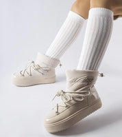 Person wearing Tharima insulated slip-on snow boots in beige with white knee-high socks, showcasing elevated platform design.