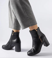Black Lyvarra insulated high-heel boots with almond toe and side zipper, paired with gray pants for elegant winter fashion.