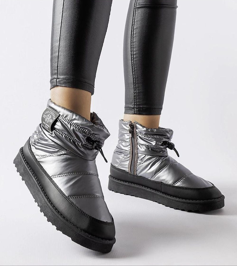 Silver insulated snow boots with side zippers and black rubber soles, paired with black leggings for winter fashion.