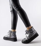 Silver insulated snow boots with side zipper and black rubber sole, worn with black leggings for a sleek winter look.