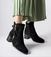 Black Esmyra low-heel ankle boots with eco leather upper and side zippers, paired with a green pleated skirt, highlighting winter style.