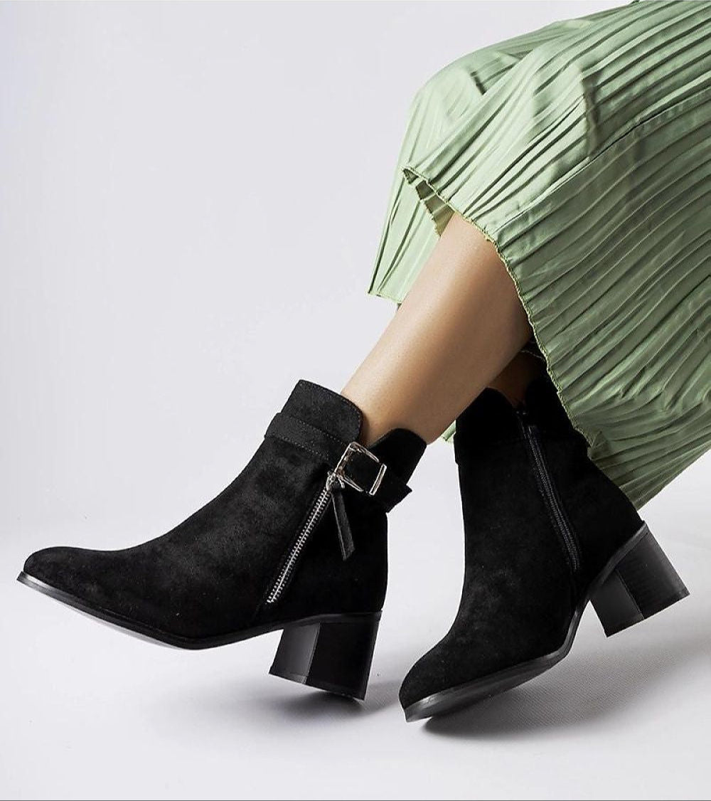 Person wearing black Esmyra low-heel ankle boots with eco leather upper and inner zipper, styled with a green pleated skirt.