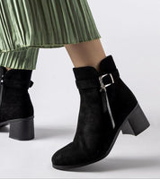 Esmyra low-heel ankle boots in black eco leather with zipper and buckle detail, paired with a green pleated skirt, side view.