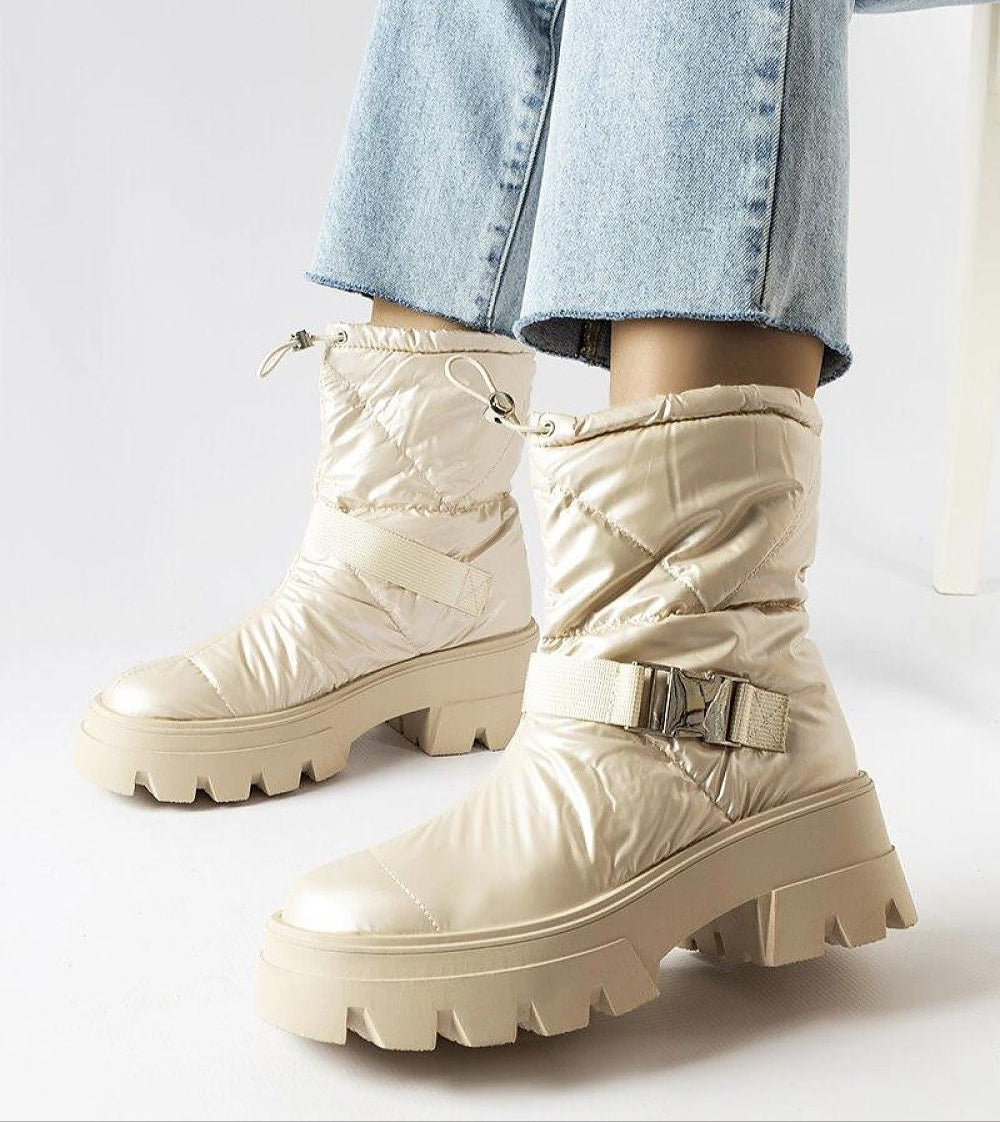 Stylish beige winter snow boots with chunky soles and adjustable straps, paired with light blue jeans for a trendy cold-weather look.