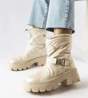 Stylish beige winter snow boots with chunky soles and adjustable straps, paired with light blue jeans for a trendy cold-weather look.