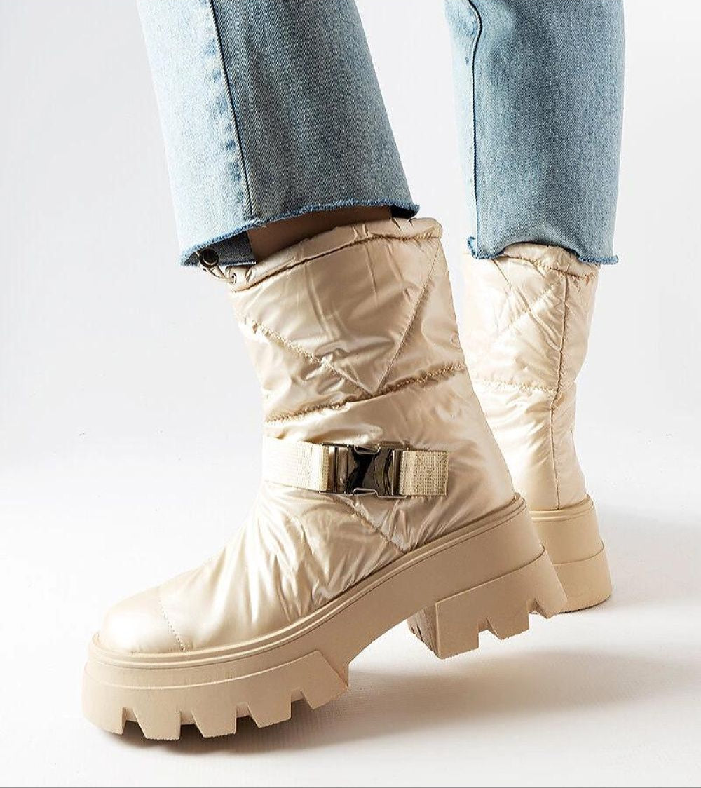 Beige quilted winter boots with thick soles and buckle detail, styled with light blue jeans.