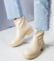 Woman wearing Lirvane zip-back ankle boots in faux leather with thick sculpted sole, paired with light denim jeans on marble floor.