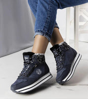 Person wearing Naverra insulated winter sneakers with fur lining, synthetic leather upper, and thick white sole, on white floor.