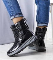 Person wearing black opalescent Orymira insulated platform snow boots with plush fur lining and sleek design in winter setting.