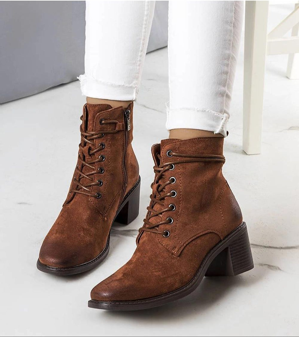 Brown square-toe heeled boots with braided lacing, worn with white jeans, showcasing autumn style and elegant suede-effect finish.