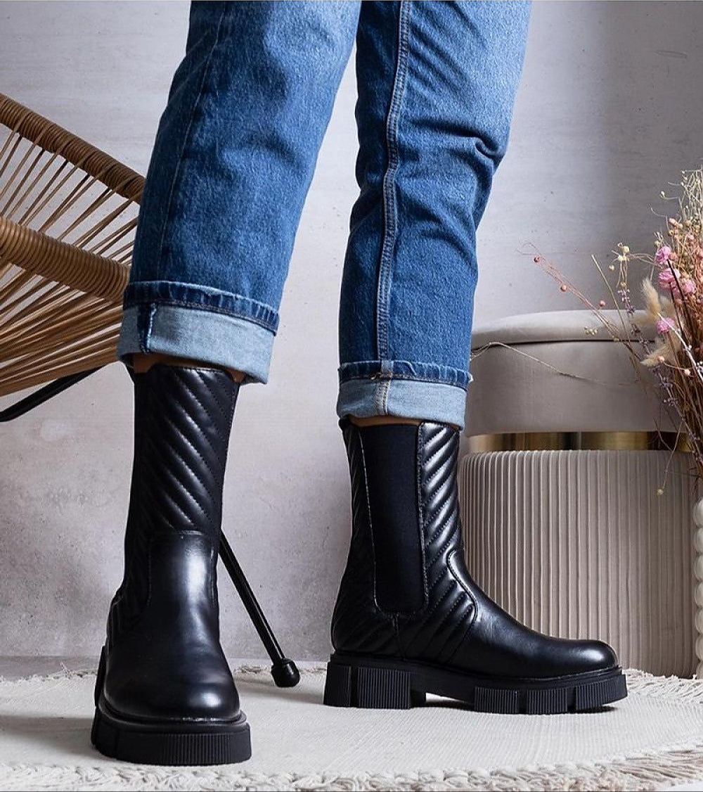 Person wearing Zarelda treaded ankle boots with thick soles and block heels, styled with rolled jeans and a cozy setting.
