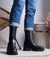 Person wearing Zarelda treaded ankle boots with thick soles and block heels, styled with rolled jeans and a cozy setting.