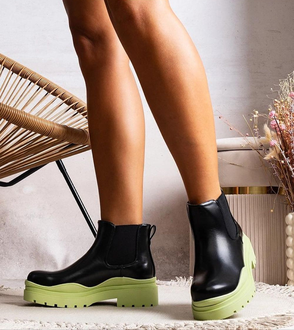 Woman wearing Tharelle slip-on ankle boots in black vegan leather with green sole and elastic side inserts for a stylish look.