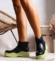 Woman wearing Tharelle slip-on ankle boots in black vegan leather with green sole and elastic side inserts for a stylish look.