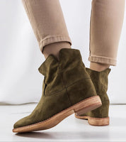 Olive suede wedge ankle boots with subtle lift and sleek design, worn with beige pants, ideal for autumn fashion.