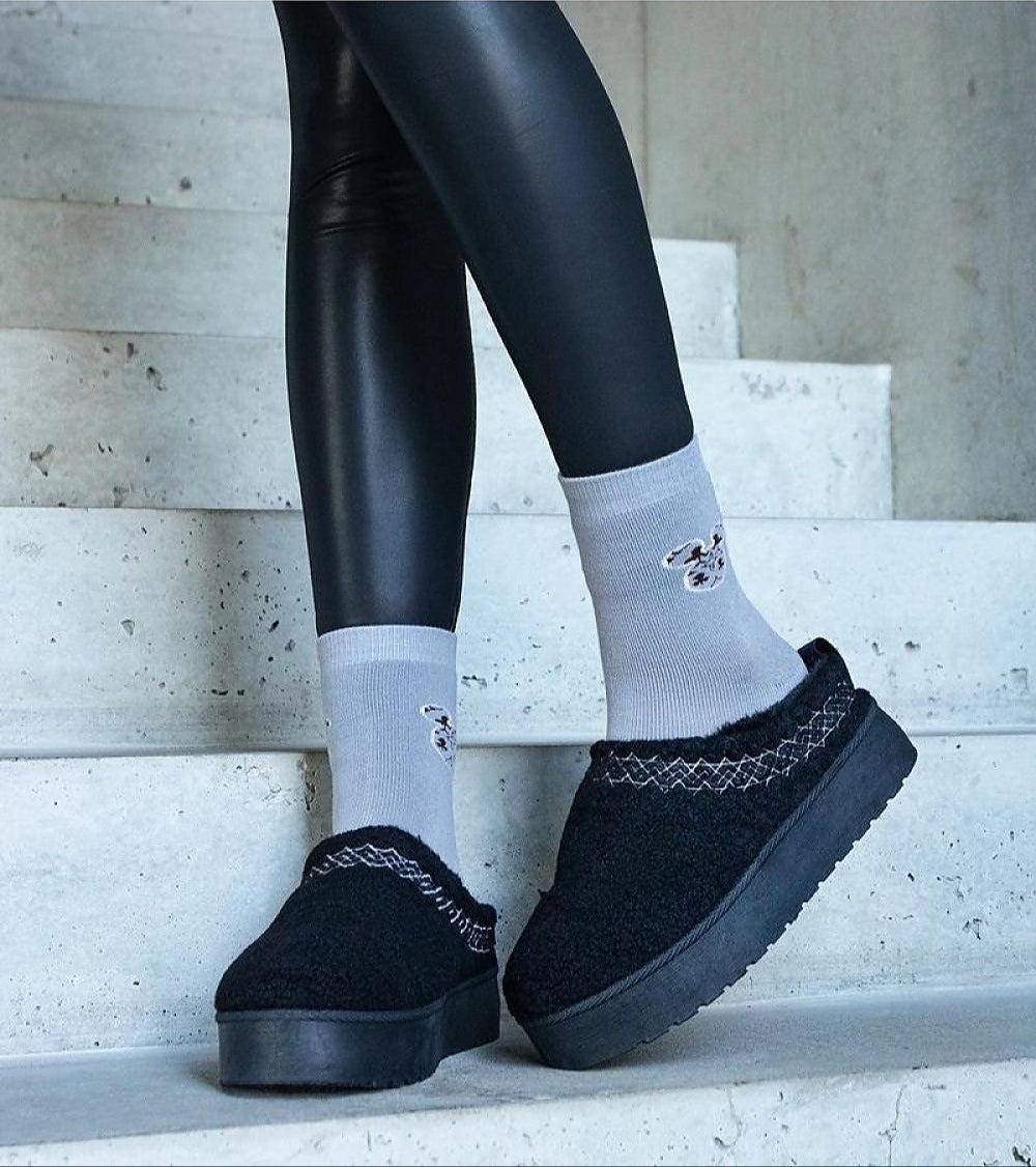 Person wearing black slip-on snow boots with embroidered detailing, paired with grey socks, standing on concrete steps.