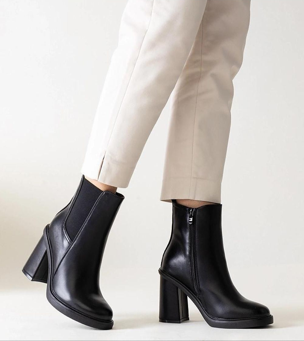 Selvina black stiletto zip-up boots in eco leather with sleek profile and high heel, paired with beige pants for elegant style.