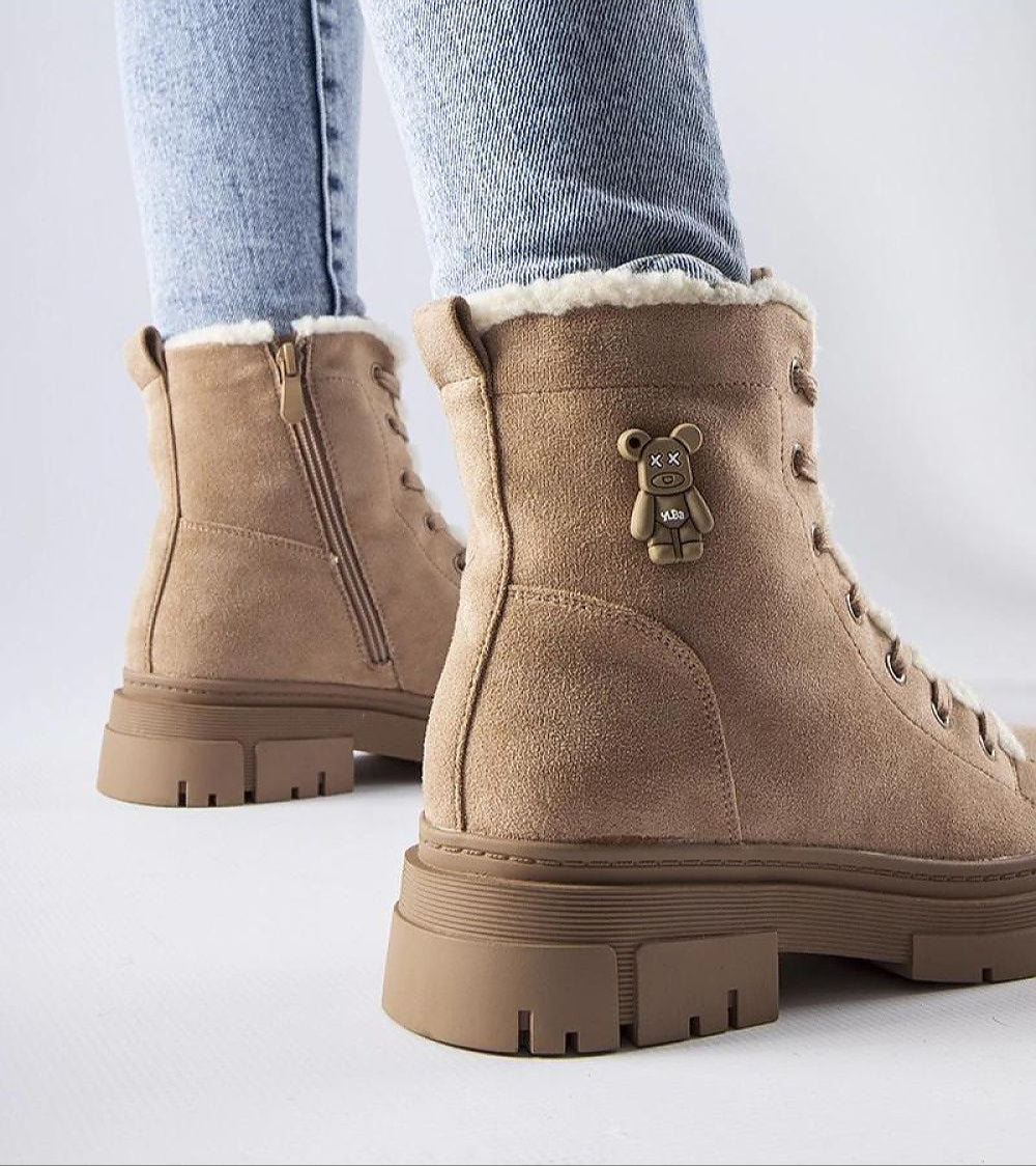 Tan suede platform boots with teddy bear charm, side zipper, and furry lining, worn with light denim jeans on a white background.