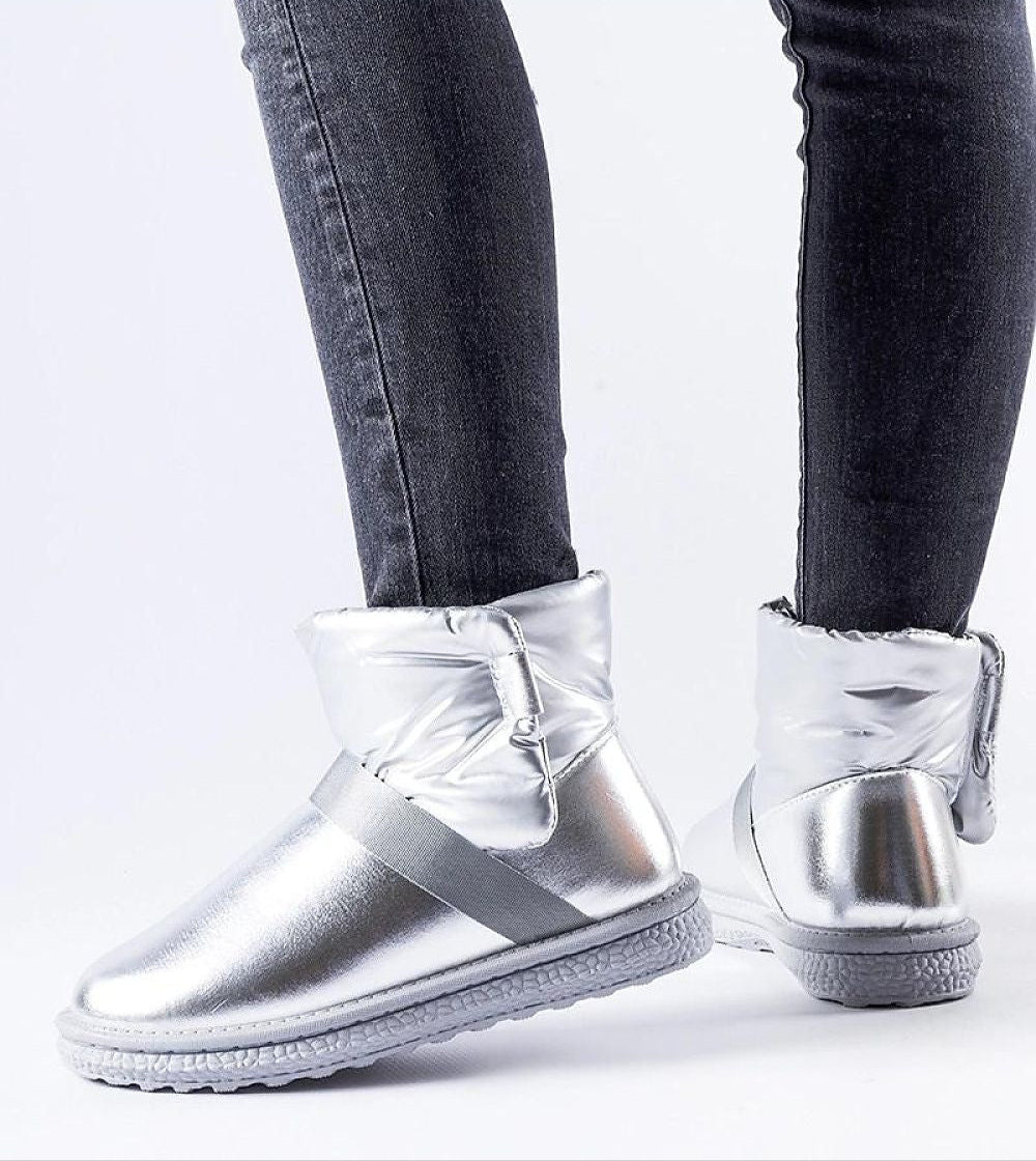 Glossy silver Velcro snow boots with rounded toe and platform, worn with dark jeans, showcasing stylish winter footwear.
