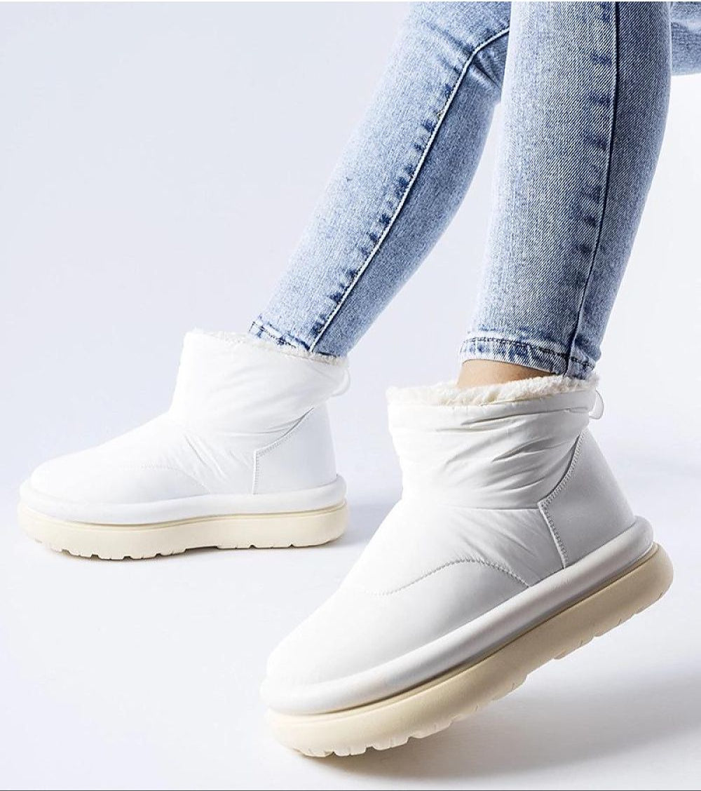 Person wearing white insulated platform snow boots with jeans, showcasing sleek slip-on design and durable sole for winter elegance.