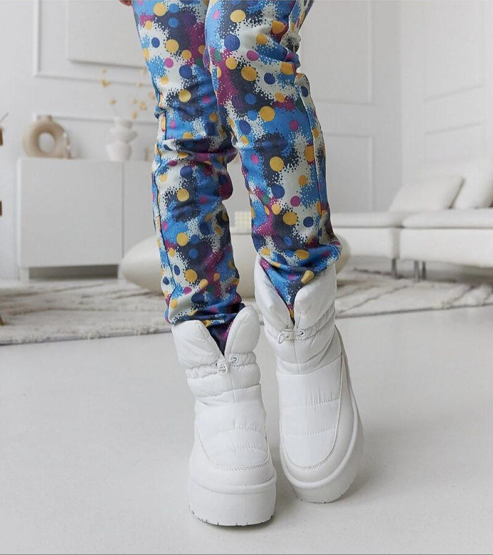 Model wearing Olviera Slip-On Platform Snow Boots with vibrant patterned pants in a modern living room.