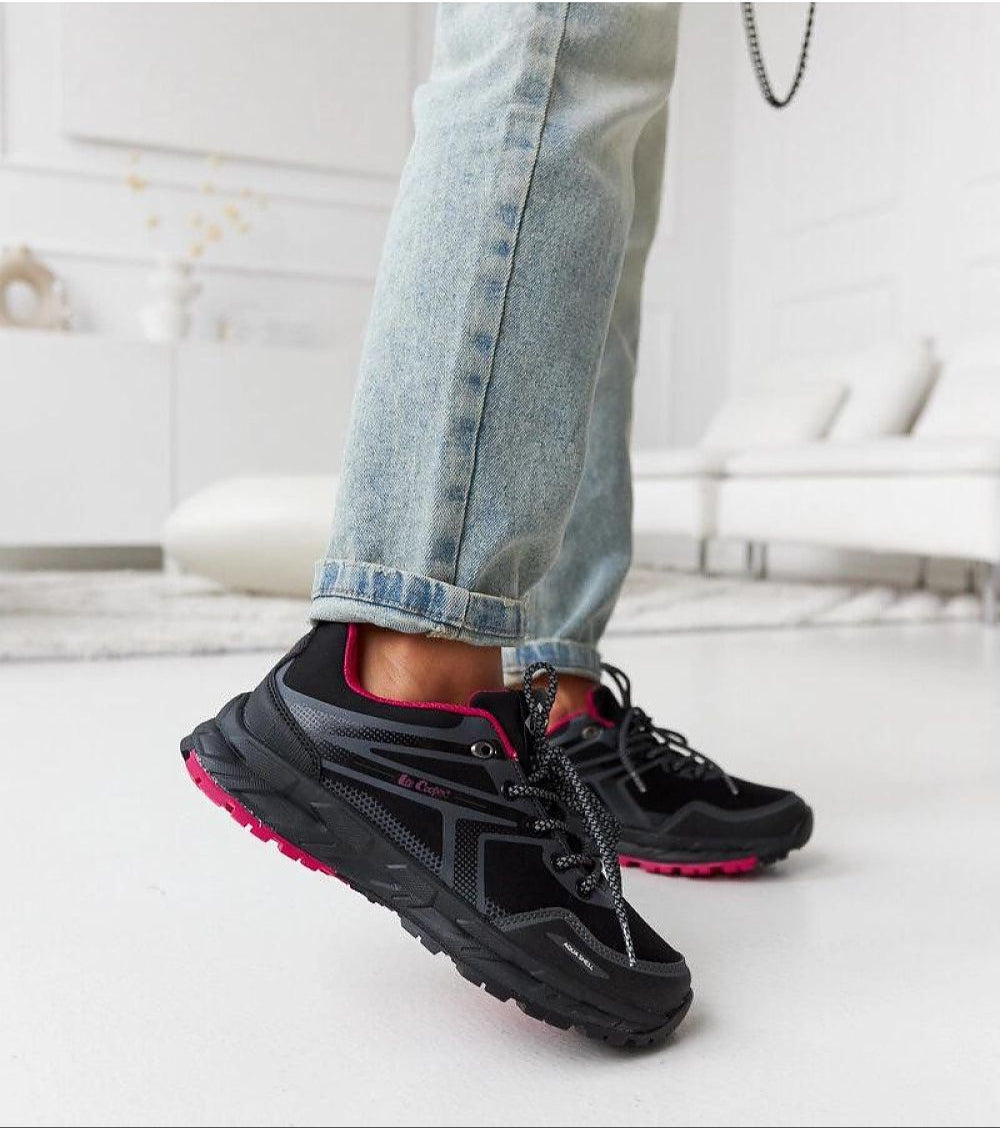 Casual style black sneakers with pink accents on person wearing jeans in modern room setting.