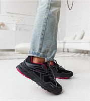 Casual style black sneakers with pink accents on person wearing jeans in modern room setting.