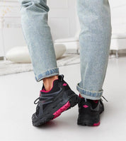 Person wearing black and pink Norvina Insulated Winter Sneakers with jeans in a cozy living room setting.