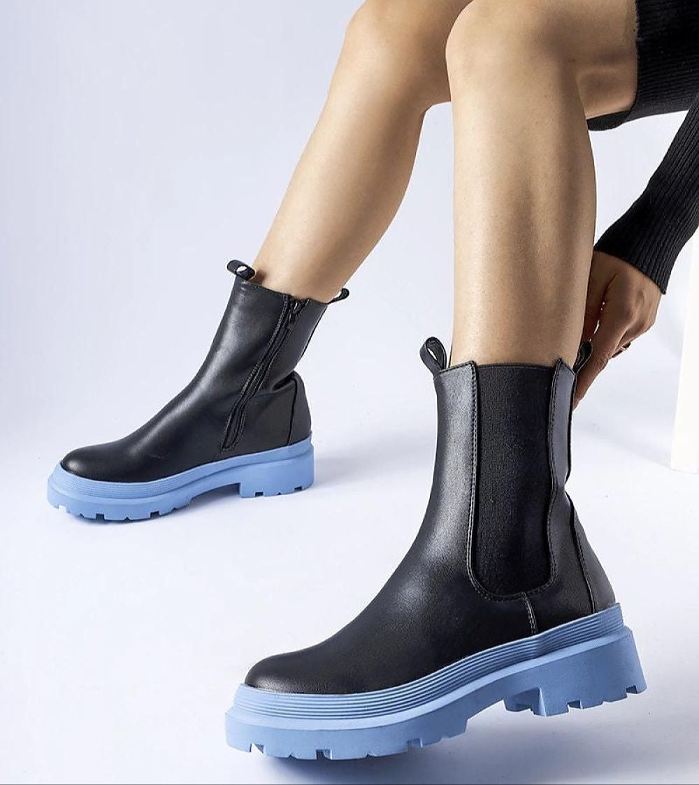 Person wearing Vereliane ankle boots with vegan leather upper and blue rubber soles, showcasing modern style and functionality.