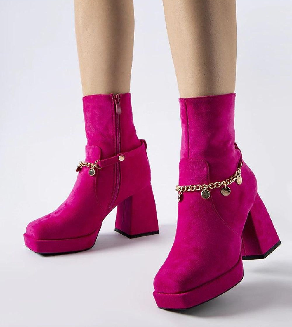 Bright pink high-heeled ankle boots with a gold chain detail showcasing modern fashion style.