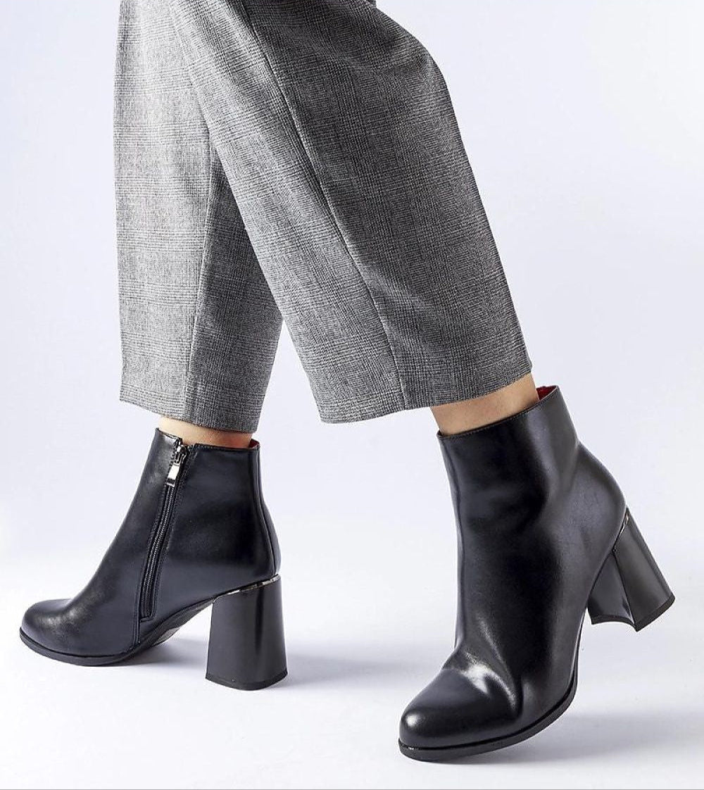 Person wearing black leather ankle boots with block heels and zipper, paired with gray plaid trousers.