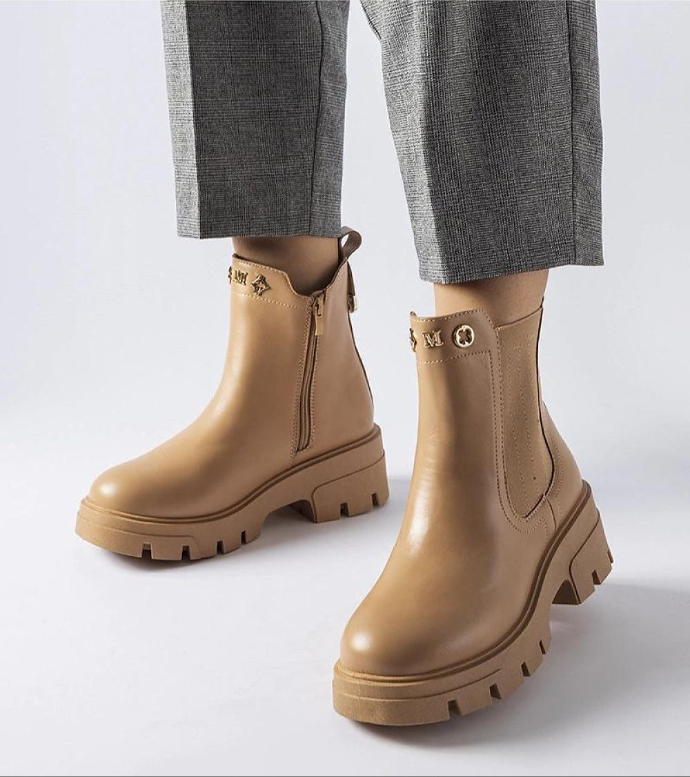 Person wearing stylish brown Medanira platform insulated boots with gray pants, highlighting side zipper and chic design.