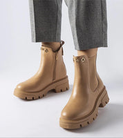 Person wearing stylish brown Medanira platform insulated boots with gray pants, highlighting side zipper and chic design.