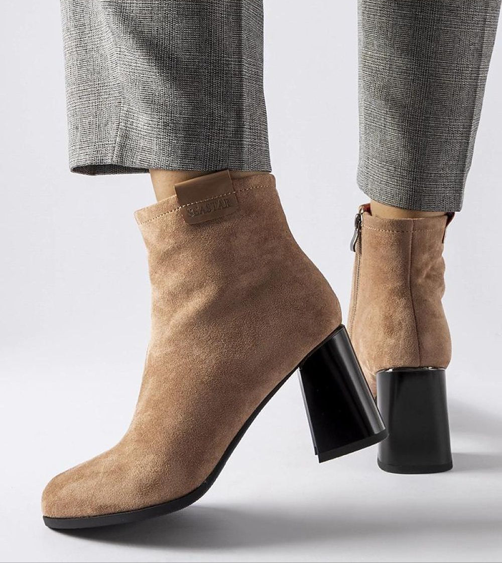 Beige suede ankle boots with block heels, featuring a side zipper and worn with grey checkered pants.