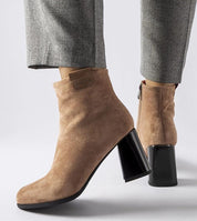 Beige suede ankle boots with block heels, featuring a side zipper and worn with grey checkered pants.