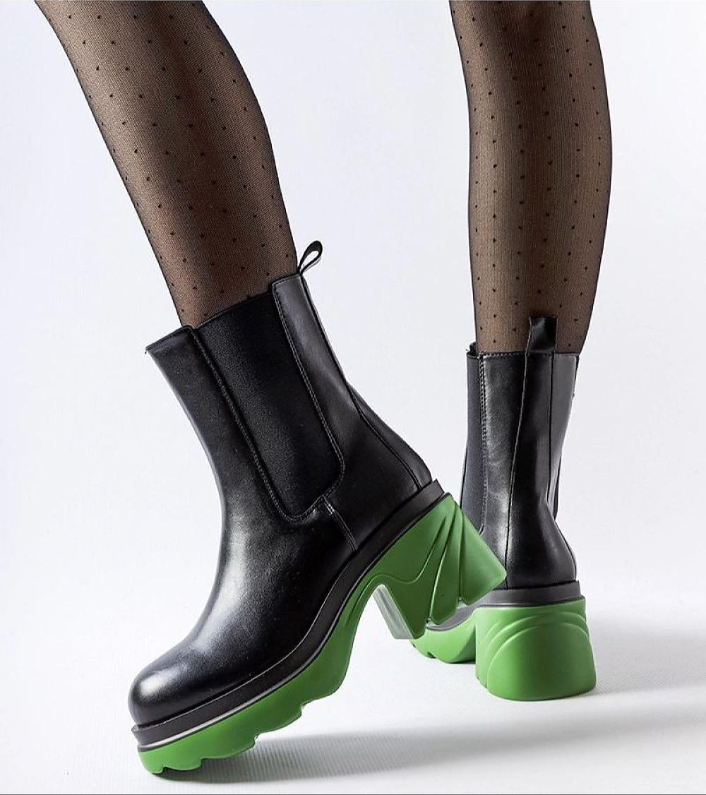 Black high-heel winter boots with vibrant green contrasting heel, worn with dotted tights, showcasing a modern stylish look.