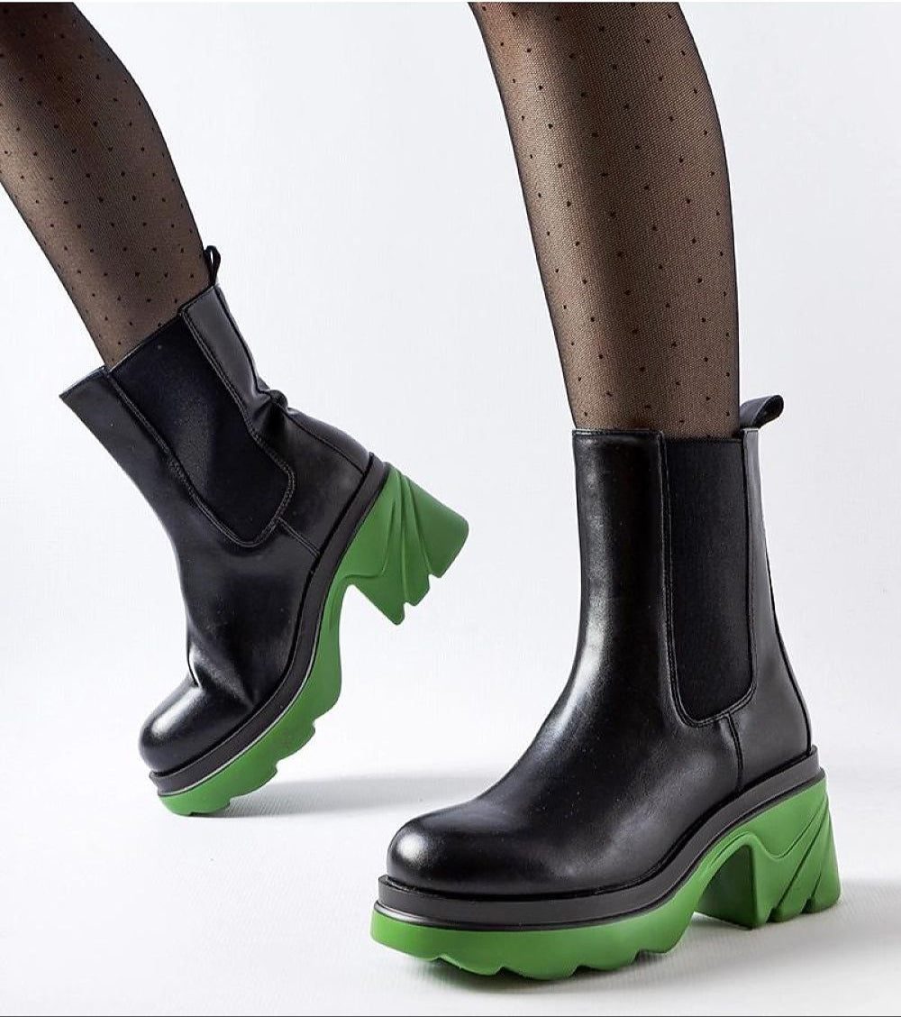 Black leather boots with green chunky soles worn with sheer tights, highlighting modern winter fashion.