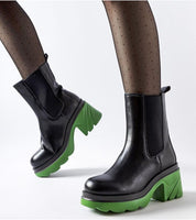 Black leather boots with green chunky soles worn with sheer tights, highlighting modern winter fashion.