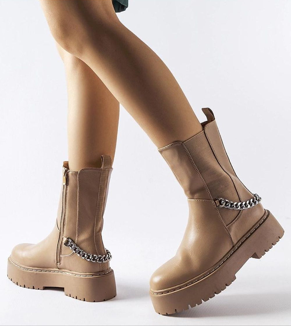 Person wearing Guglielmo chain-trimmed flat boots with beige rubber sole and gold-tone chain embellishment.