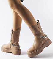 Person wearing Guglielmo chain-trimmed flat boots with beige rubber sole and gold-tone chain embellishment.
