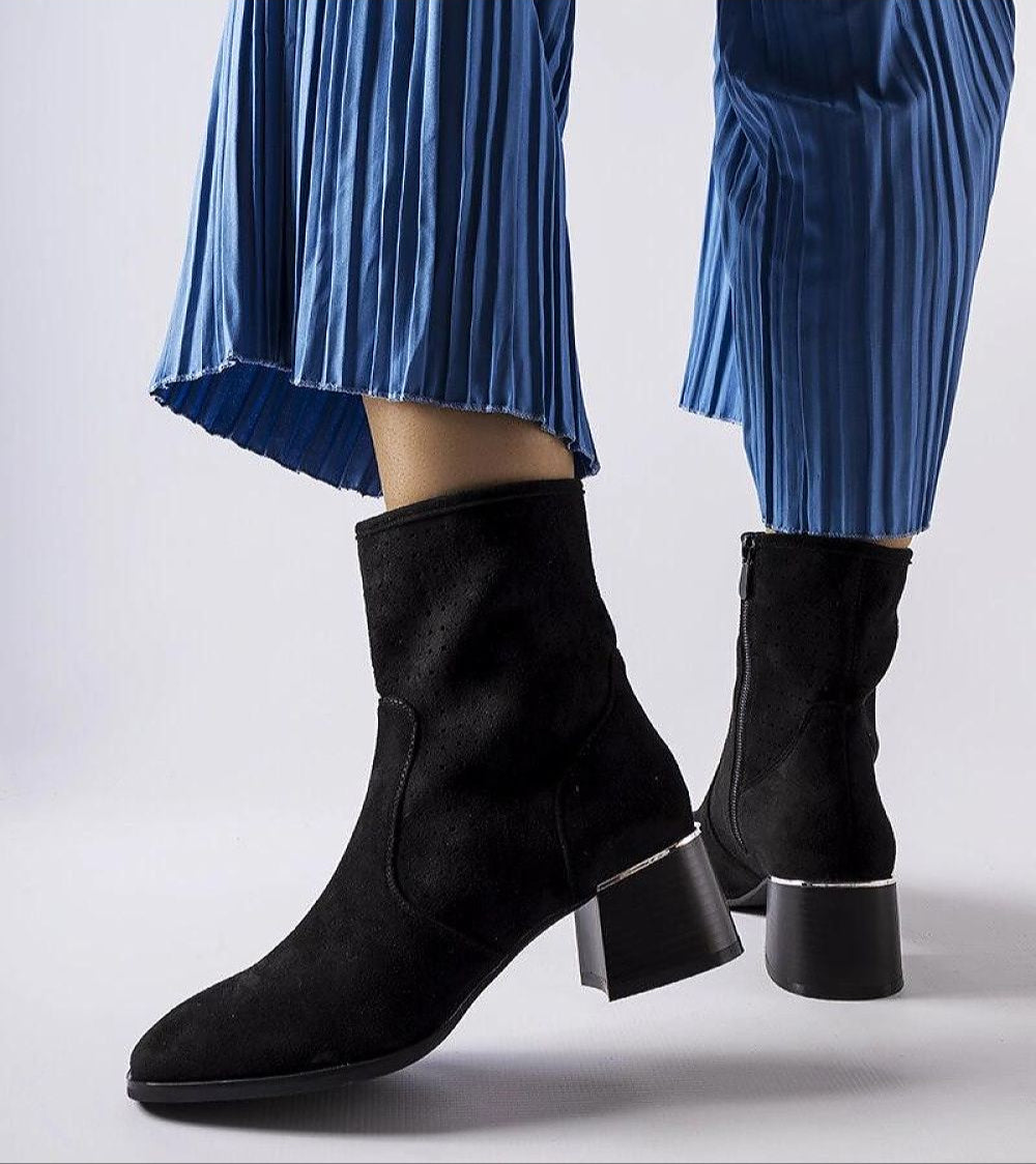 Black perforated zip-up ankle boots with a flat heel, styled with blue pleated pants for a chic, modern look.