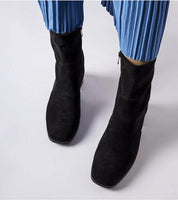 Model wearing Soretta Perforated Zip-Up Boots in black eco-leather with blue pleated skirt.