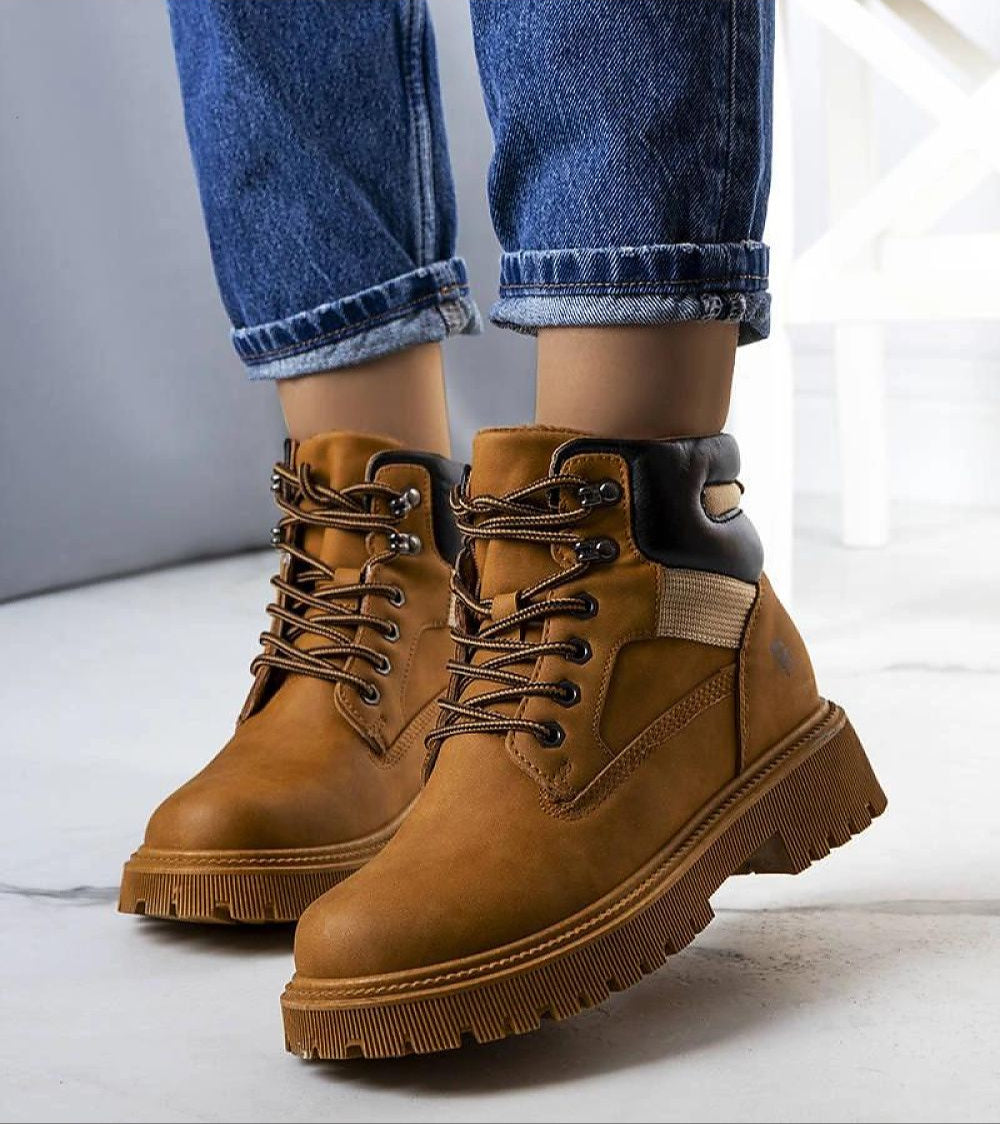 Brown leather trapper boots with faux fur lining and lace-up front, perfect for winter adventures, worn with denim jeans.