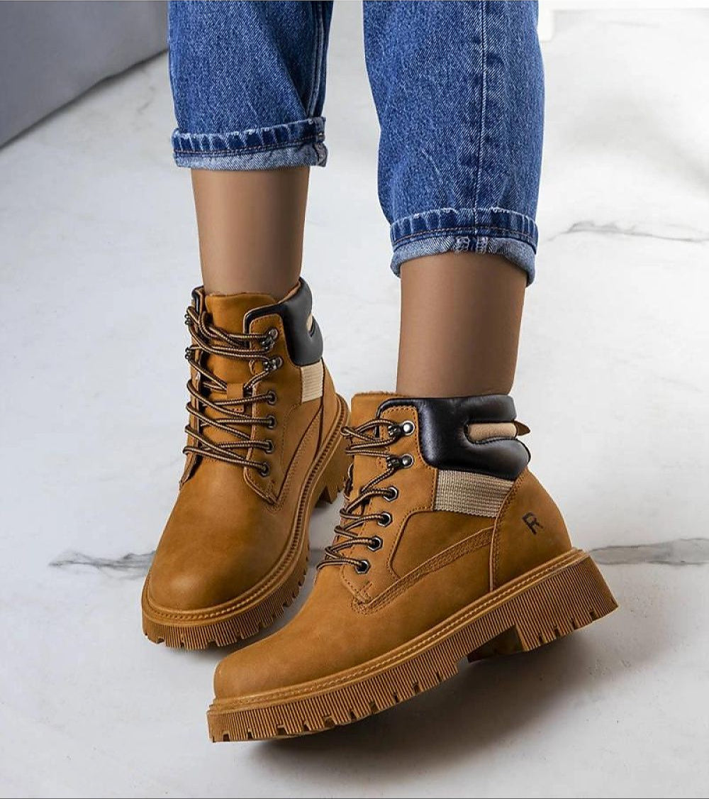 Person wearing brown leather trapper boots with fur lining, suitable for winter adventures; paired with blue jeans on a marble floor.