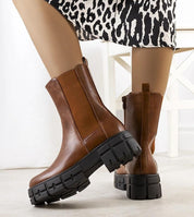 Woman wearing Ferensa Brown Tall Boots with chunky black sole and side zip, styled with a patterned skirt for a chic look.