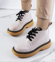Person wearing Redelek white matte lace-up boots with yellow rubber soles on a marble floor.