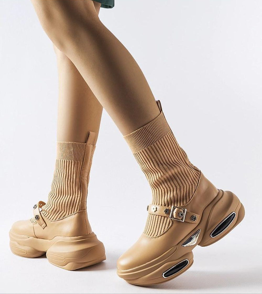 Close-up of beige Elvessa stretch knit ankle boots with ribbed sock-like shaft and sculpted heels, worn by a person.