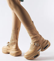 Close-up of beige Elvessa stretch knit ankle boots with ribbed sock-like shaft and sculpted heels, worn by a person.